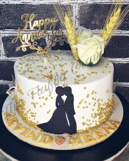 An anniversary cake with gold pearls and a hand-cut couple silhouette