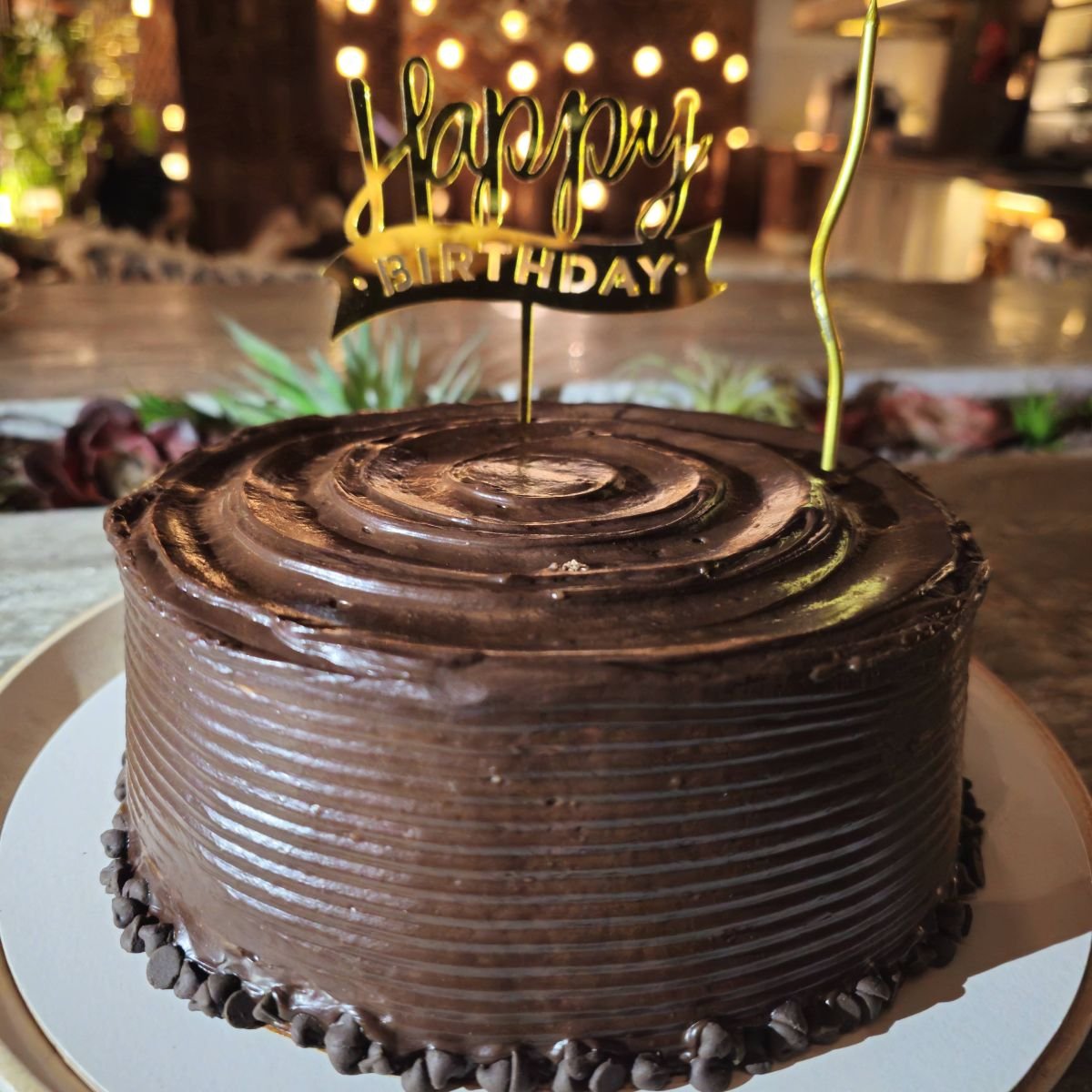 A chocolate truffle birthday cake ringed with chocolate chips and finished with a gold topper