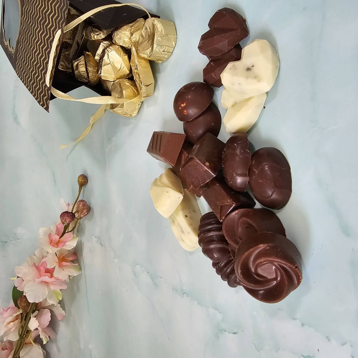 Handcrafted chocolates spilling from a gold-wrapped gift box on marble