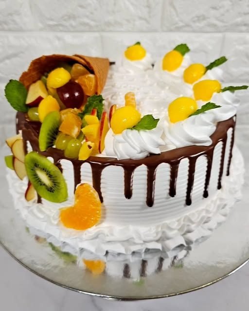 A fresh fruit cake with a chocolate drip and a sugar cone spilling seasonal fruit