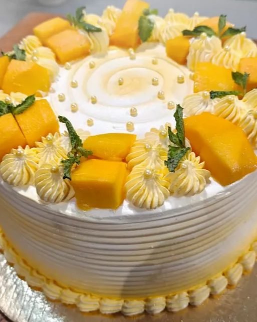 A mango celebration cake ringed with piped cream and gold pearls