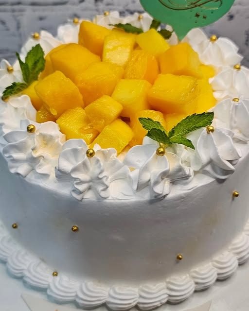 A cream cake crowned with fresh mango cubes and mint leaves
