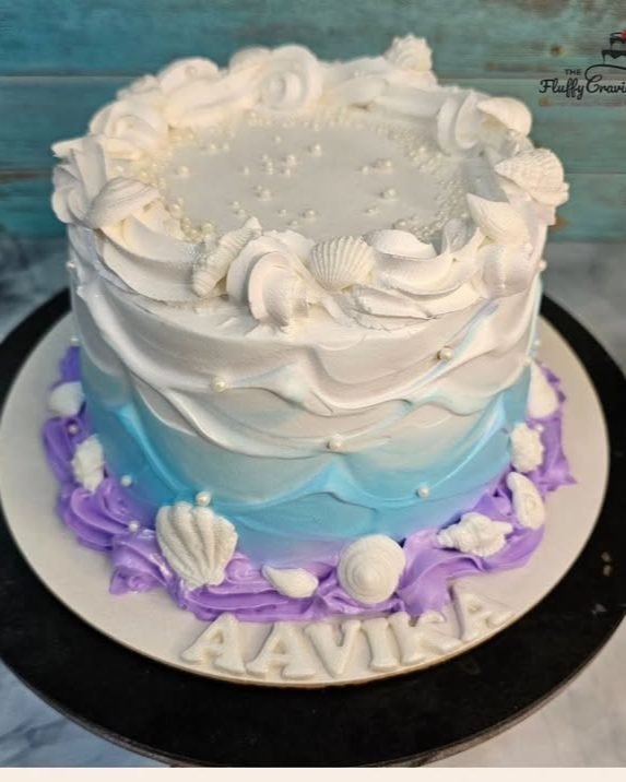 An ocean-ombre cake in white, blue and lilac with piped seashells