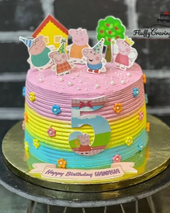 A pastel rainbow-striped cartoon theme cake with a sculpted number five