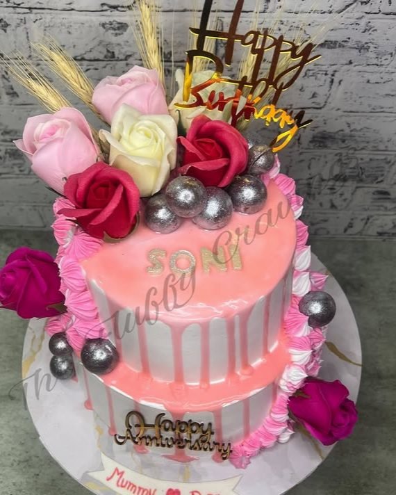 A two-tier pink drip cake dressed with fresh roses and hand-piped ruffles