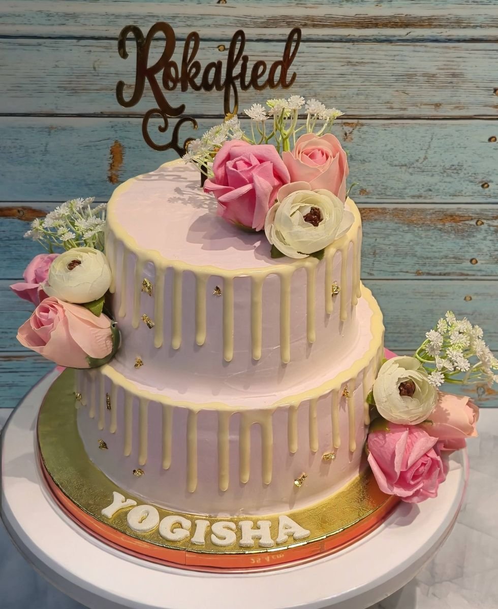 A two-tier blush pink cake with a white chocolate drip and fresh roses