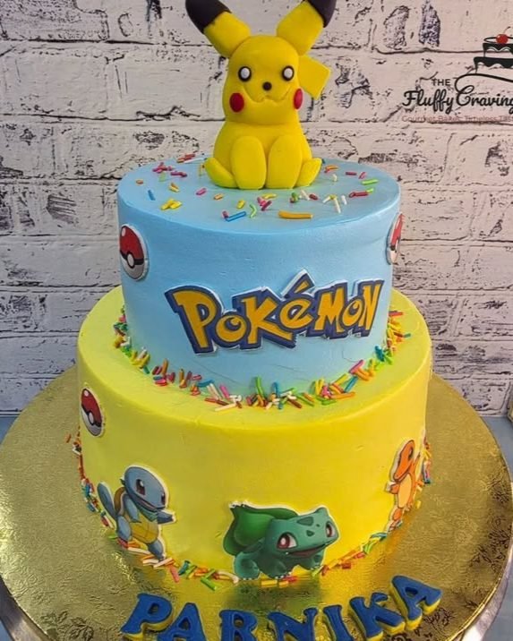 A two-tier blue and yellow cartoon-theme birthday cake with a modelled topper